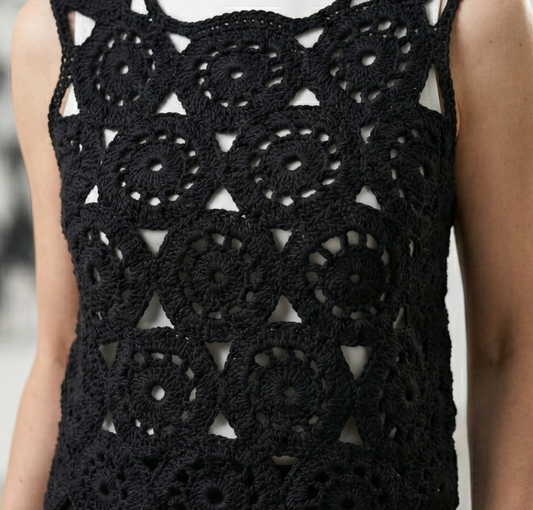 Front view of a model wearing the black Eclipse Circles crochet top over a white turtleneck, featuring geometric circular motifs and a scalloped hem.