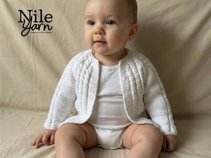 Baby wearing a white knitted cardigan sitting on a beige surface with 'Nile Yarn' branding.