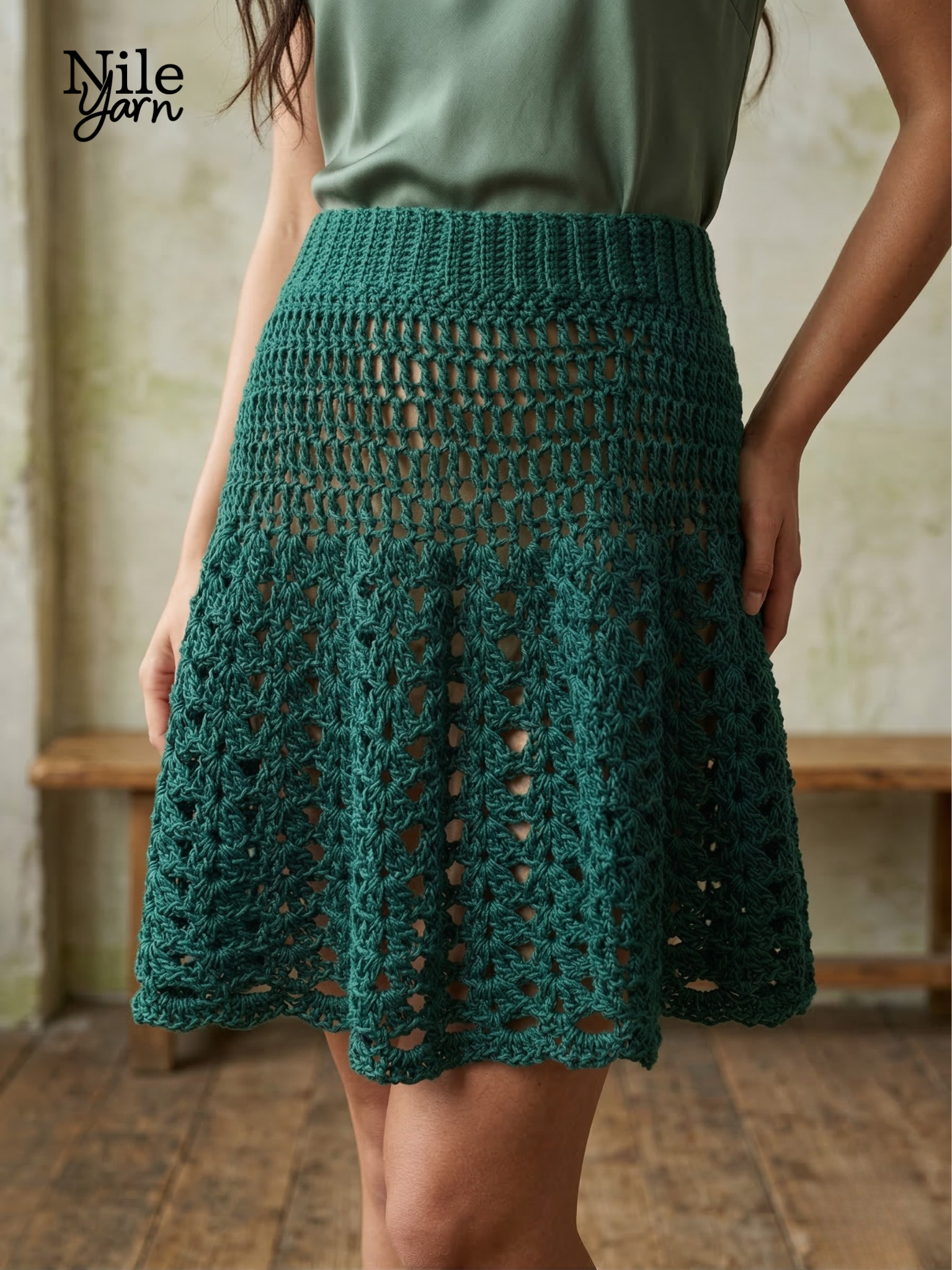 Front view of the Palm Grove Skirt, a knee-length green crochet skirt with a textured V-stitch design and a ribbed waistband. Nile Yarn Branded